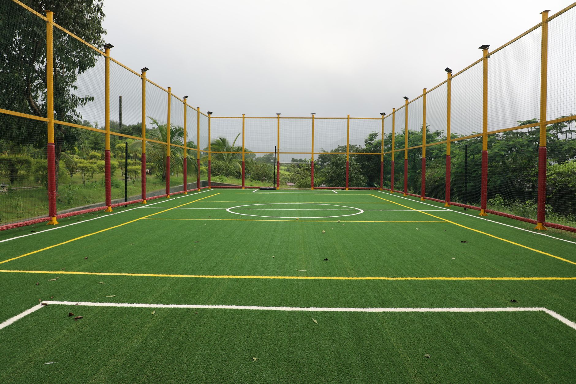 Vibrant outdoor futsal court with artificial turf surrounded by a net in a lush setting.